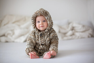 Little baby boy playing at home in bed, dressed in hand made knitted overall