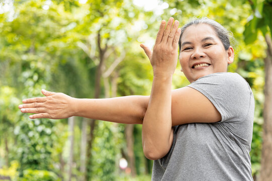 Old senior woman stretching shoulder muscle, exercising in green park, breathing clean air, good and healthy life quality, self care and wellness concept image