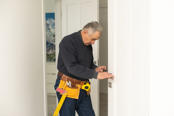 Ordinary elderly man independently repairs a door