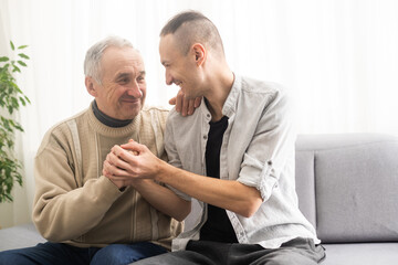 Fototapeta premium Young adult caucasian son listening and supporting his old elderly senior father at home indoors. Care and love concept.