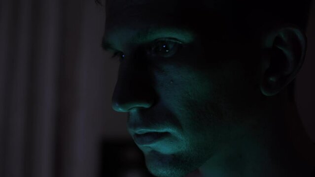 Portrait of a male hacker. nervous look. dark room. blue light.