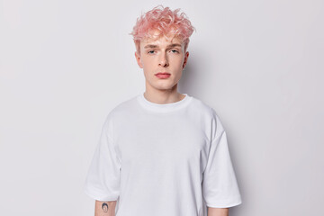 Portrait of attentive hipster guy with pink hair and tattoo on arm dressed in casual basic t shirt...