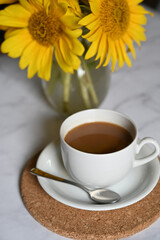 Morning coffee. Cozy composition: a cup of coffee on an open book, a blue sweater and sunflower flowers on a concrete background. Still life concept. Copy space.