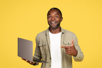 Happy mature black man in casual showing finger at computer, chatting in social networks