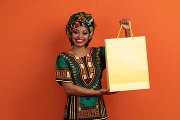 Happy traditional african woman holding yellow blank paper shopping bag