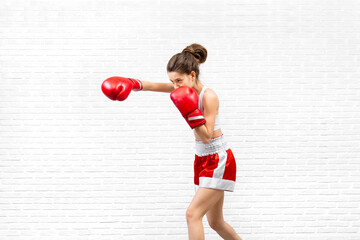 Attractive caucasian young woman in red boxing gloves and boxer shorts practice a punch on loft...