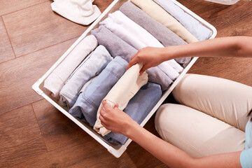 Women's hands neatly fold clothes into a metal basket. The concept of tidying up, cleaning,...
