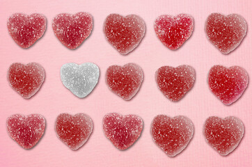 Obraz na płótnie Canvas Heart shaped candy in rows with a special one sticking our on pink paper | sugar coated jelly hearts