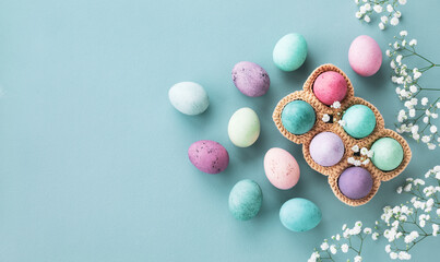 Easter greeting card with pastel easter eggs decorated white flowers on blue table top view.