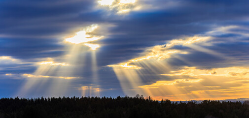 Rays of sunlight break through a dense cloud cover over a wooded landscape near Ravensburg in...