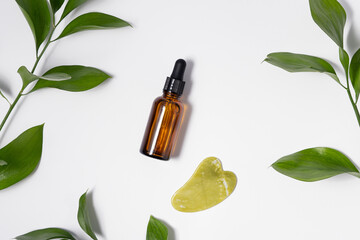 Close-up of skin serum and green quartz gouache massager on white isolated background with plant...