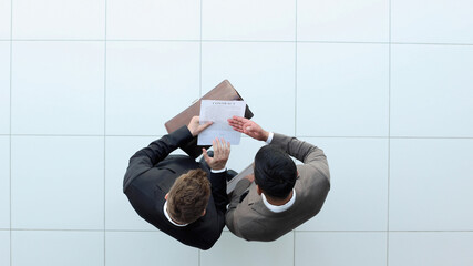 Two businessman signing an agreement. One hand holds the document and the other signs.