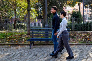 The young couple is holding hands. Young couple is walking in a park in Rome.