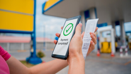 Woman using contactless payment by mobile phone with QR code at car filling station