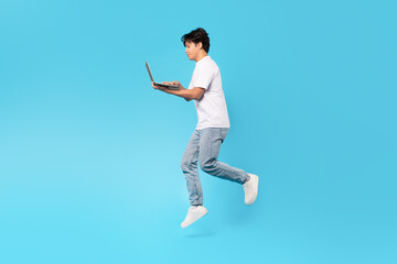Asian Teen Boy Holding Laptop Jumping Browsing Internet, Blue Background