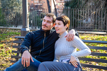 Young couple is sitting on a bench in the park in Rome. Beautiful couple is embracing themselves in the park. - 575648639