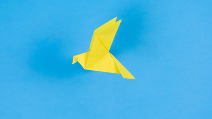 Yellow paper origami dove flies. Blue background. Symbol of peace.