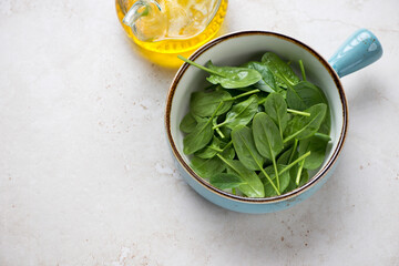 Fresh spinach in a turquoise serving bowl, high angle view on a light-beige stone background, horizontal shot with space