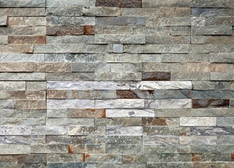 Stone wall paneling made of stacked stripes rock bricks. The colors are white, brown, and gray. Texture.