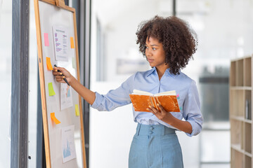 young asian entrepreneur of small company putting a adhesive sticky notes and graph chart on...