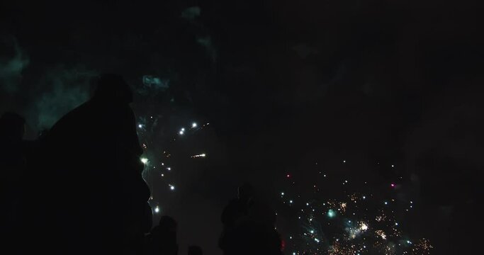 Wystrzał sztucznych ogni w Sylwestra. Eksplozje na niebie,  stojący ludzie w nocy. 