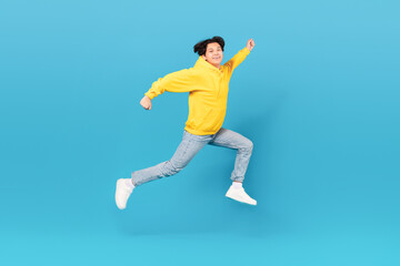 Fototapeta na wymiar Japanese Teen Boy Jumping In Mid Air Over Blue Background