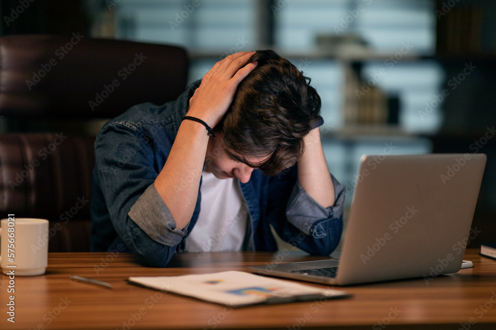 Poster exhausted man sitting in front of computer at dark office