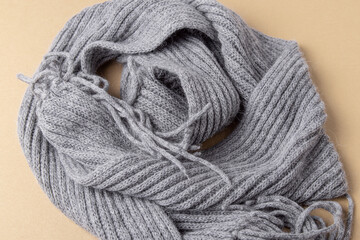 Fototapeta na wymiar Grey knitted scarf on beige background. Soft material
