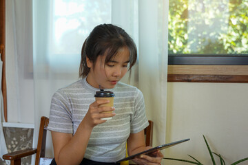 Asian woman holding coffee cup Happy to work outside She uses a tablet to search for information on the Internet..soft and selective focus