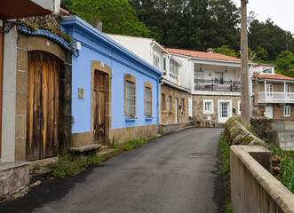 Fototapeta na wymiar Calle solitaria, asfaltada con casas de color azul y árboles verdes en el pueblo del Ferrol, La Coruña, verano de 2021
