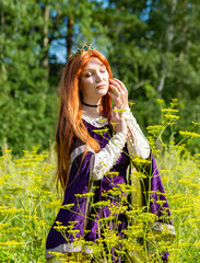 Portrait of woman dancing in flower field outdoors. Flirty girl with long red hair turning around in spring park. Closeup young female person feeling free in blooming garden in summer day.