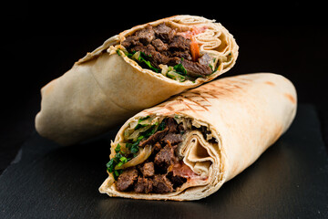 Shawarma from beef, tomatoes, herbs, sauce and pita bread on a dark background. - 575676499