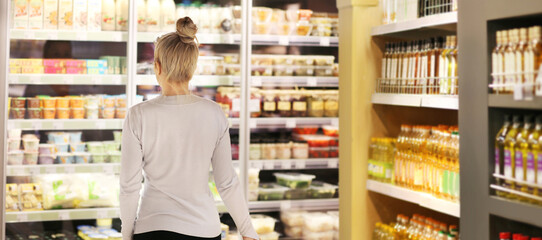 Woman choosing frozen food from a supermarket freezer, reading product information