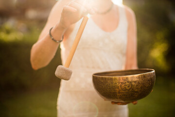 Woman playing Tibetan Singing Bowl with Mallet over Sunset Sky.Relaxing Music Therapy and Sound Healing. Peaceful Meditation and Relaxation concept.