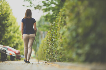 Blind woman walking on city streets, using her white cane