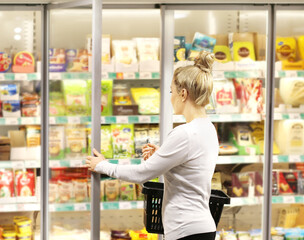 Woman choosing frozen food from a supermarket freezer, reading product information
