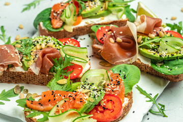 set of sandwich with cream cheese, prosciutto, avocado and fresh greens on a wooden background. Keto breakfast or snack, top view