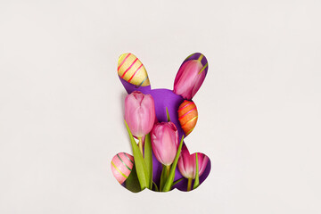 Bunny shape Easter holiday composition with pink tulips and colorful eggs, white paper background. Easter greeting card