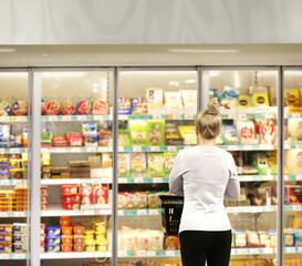 Woman choosing frozen food from a supermarket freezer, reading product information