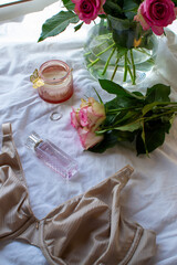 Women's bra, pink roses and perfume on a white sheet