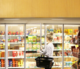 Woman choosing frozen food from a supermarket freezer, reading product information