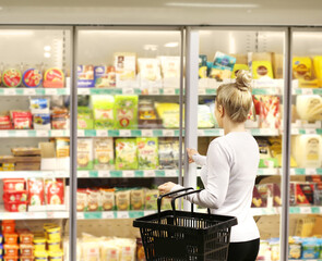 Woman choosing frozen food from a supermarket freezer, reading product information