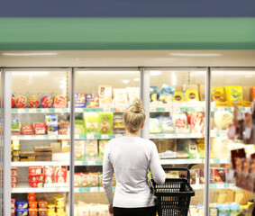 Woman choosing frozen food from a supermarket freezer, reading product information