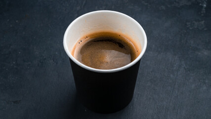 A cup of hot espresso coffee, black coffee in paper cup on dark background.