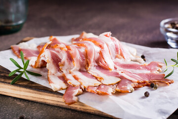 Raw smoked bacon and rosemary on a cutting board on the table. Hearty snack.