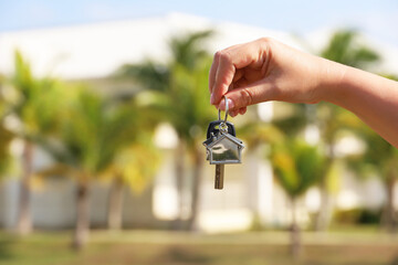 Real estate agent, home keys in female hand on background of house surrounded by palm trees. Buying...
