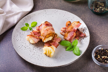 Rolls of fried bacon and mashed potatoes and basil on a plate on the table.