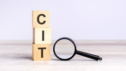 CIT - corporate income tax - text wooden cube blocks and magnifying glass on table. strategy, marketing, and content concept