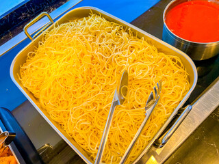 buffet - vermicelli, pasta in a large stainless steel gastronorm container. next to it is red tomato sauce in a small pot with a long handle. at catering event on some festive event, party or wedding