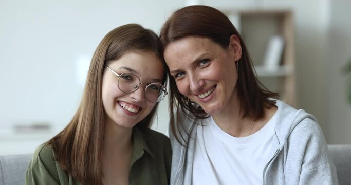 Close up happy mom and daughter smiling, hugging pose for camera, shoot at home. Cheerful caring 45s mother cuddles, kiss her teen girl, express care, feel love. Family portrait of two age generations